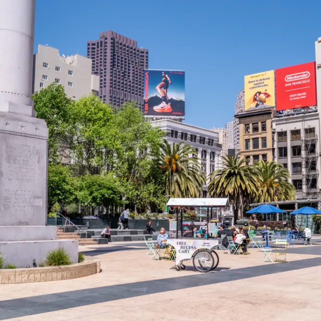 Union Square plaza with the Dewey Monument, cafe seating, and billboards on surrounding buildings