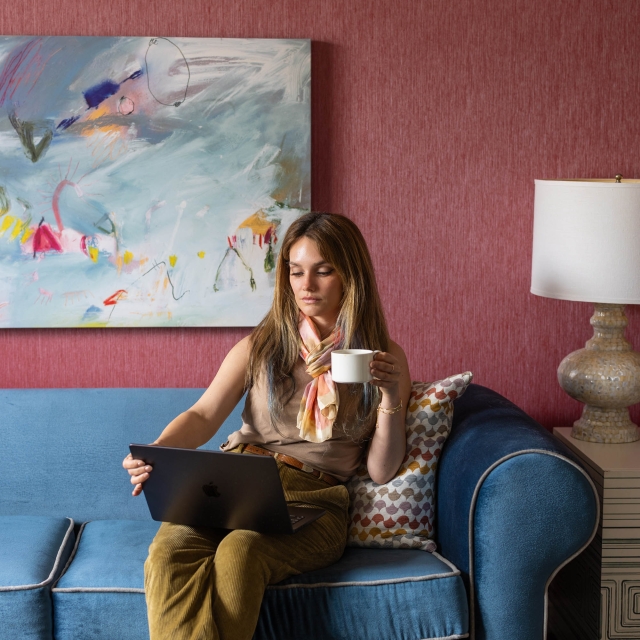 A woman looking at her laptop while holding a cup of coffee at The Marker