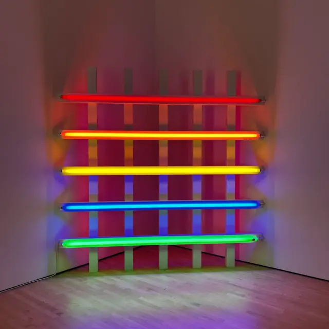 Art installation of five horizontal neon tubes in red, orange, yellow, blue, and green, glowing in a gallery corner