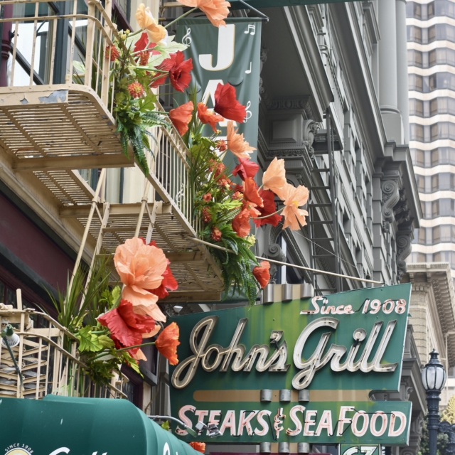 John's Grill signs and awning on a San Francisco building, decorated with large paper poppy flowers along the fire escape